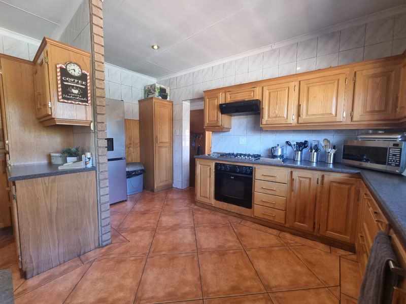 A functional kitchen featuring traditional wooden cabinetry, a built-in oven with gas hob, tiled flooring, and a distinctive brick feature wall.