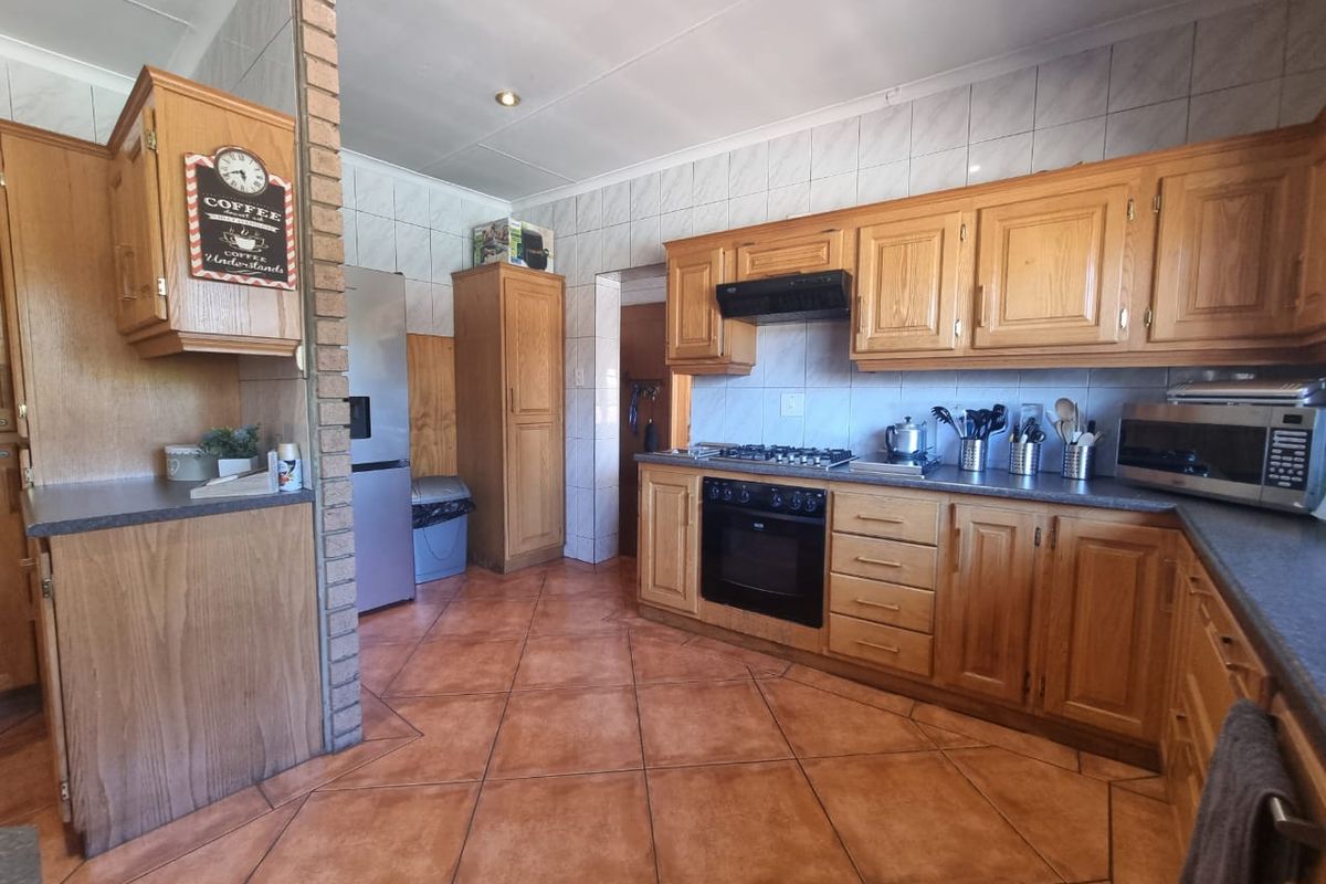 A functional kitchen featuring traditional wooden cabinetry, a built-in oven with gas hob, tiled flooring, and a distinctive brick feature wall.
