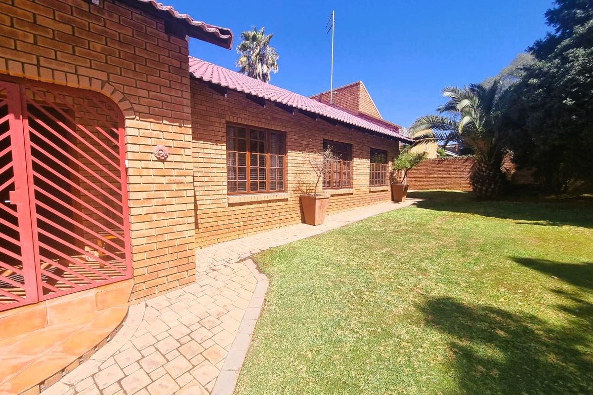 A well-maintained rear exterior view featuring a face brick facade, tiled roof, paved walkway, and a neat garden area.