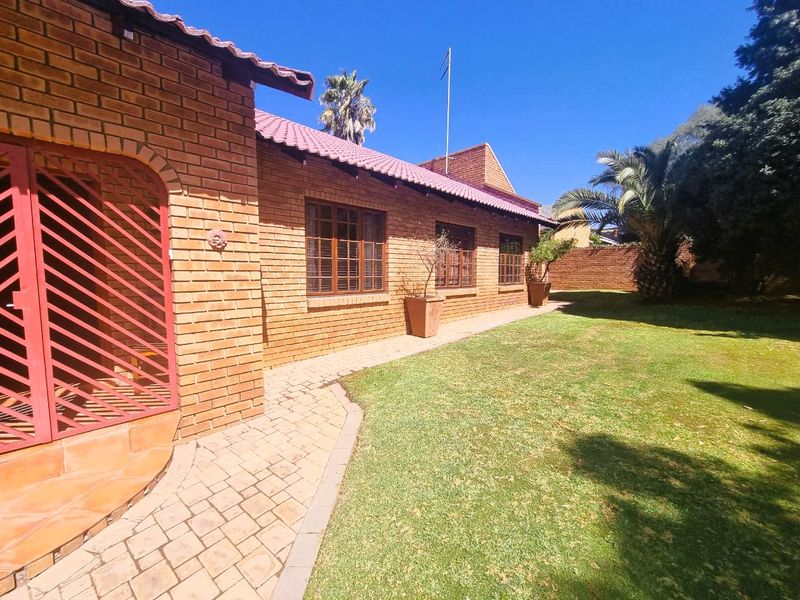 A well-maintained rear exterior view featuring a face brick facade, tiled roof, paved walkway, and a neat garden area.