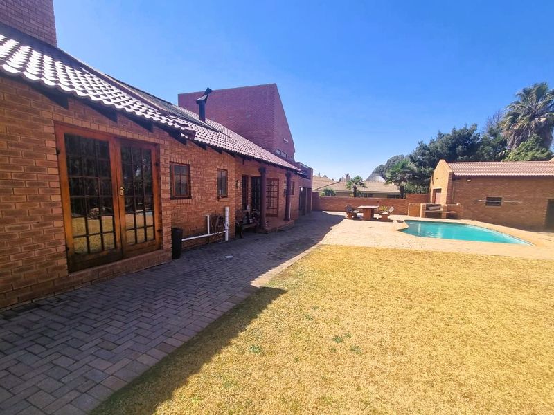 Spacious rear garden featuring a brick-faced home, paved patio area, swimming pool, and a detached outbuilding, ideal for outdoor entertaining.