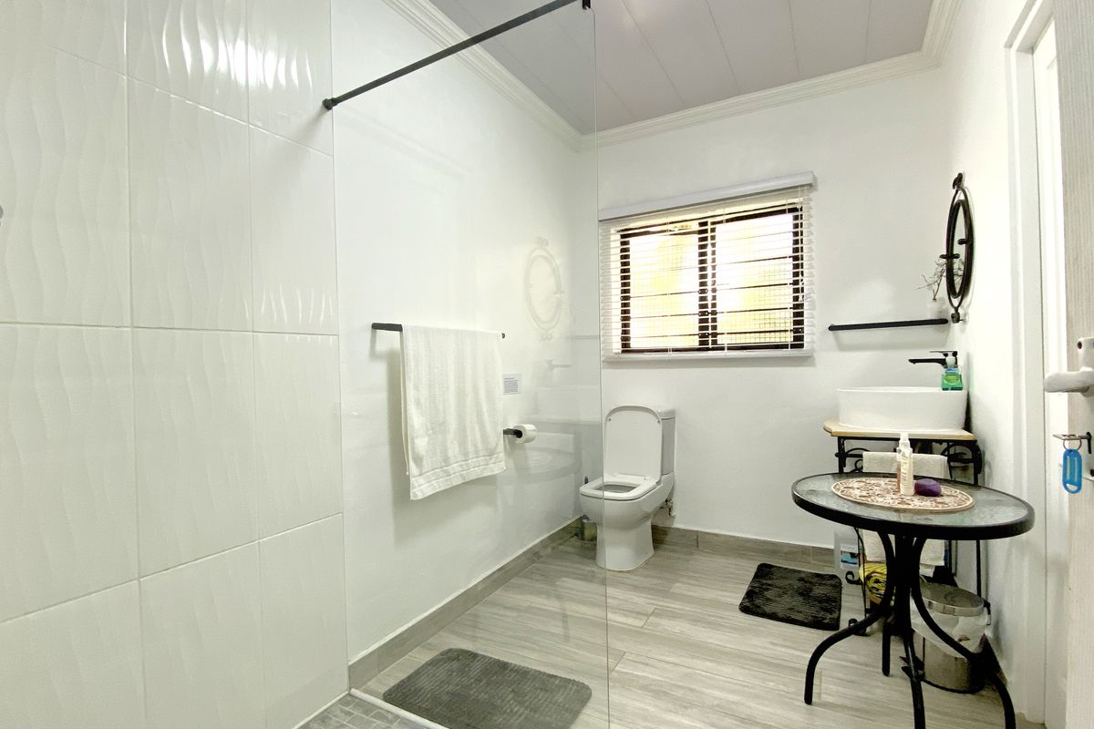 A modern bathroom featuring a walk-in glass shower enclosure, white wall tiling, a pedestal-style basin, and a toilet with wood-look floor tiles.
