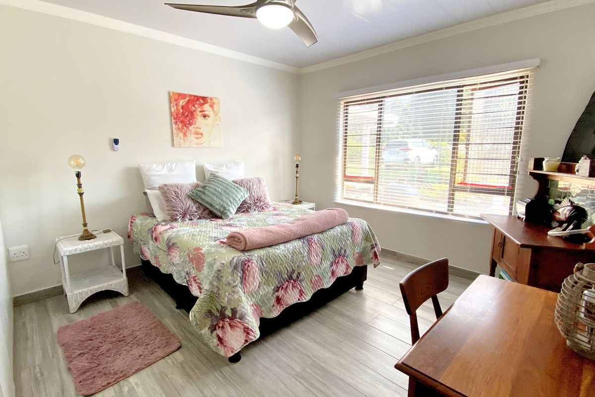 A well-lit bedroom featuring light-toned wood-look flooring, a ceiling fan, and a large window with horizontal blinds.