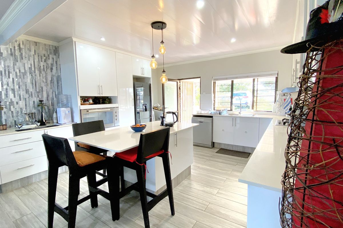 Modern kitchen featuring white cabinetry, a central island with breakfast bar seating, stone countertops, and tiled flooring with integrated lighting.