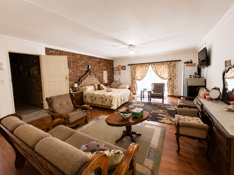 Spacious bedroom featuring an exposed brick feature wall, laminate flooring, and a ceiling fan, offering a warm and traditional aesthetic.