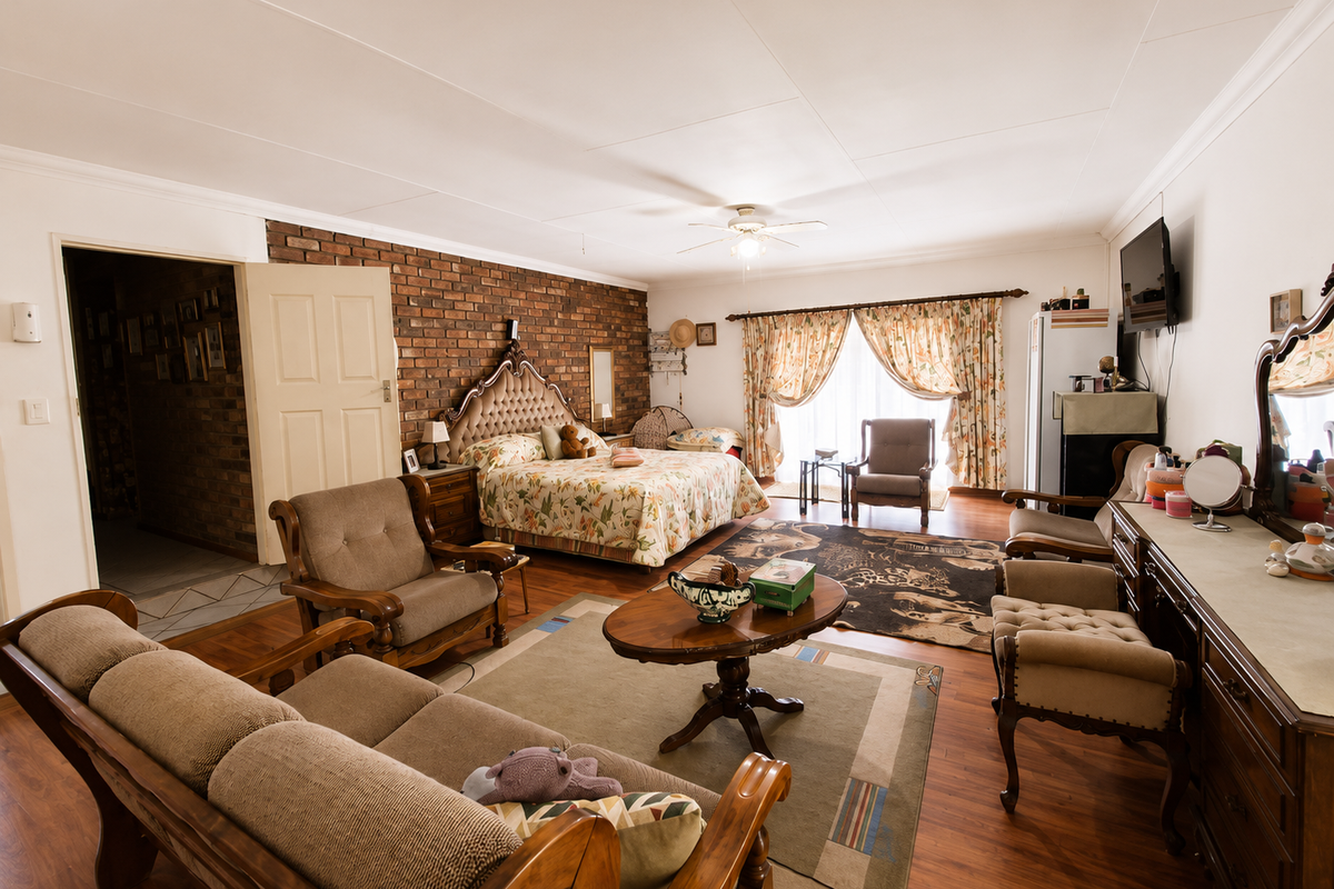 Spacious bedroom featuring an exposed brick feature wall, laminate flooring, and a ceiling fan, offering a warm and traditional aesthetic.