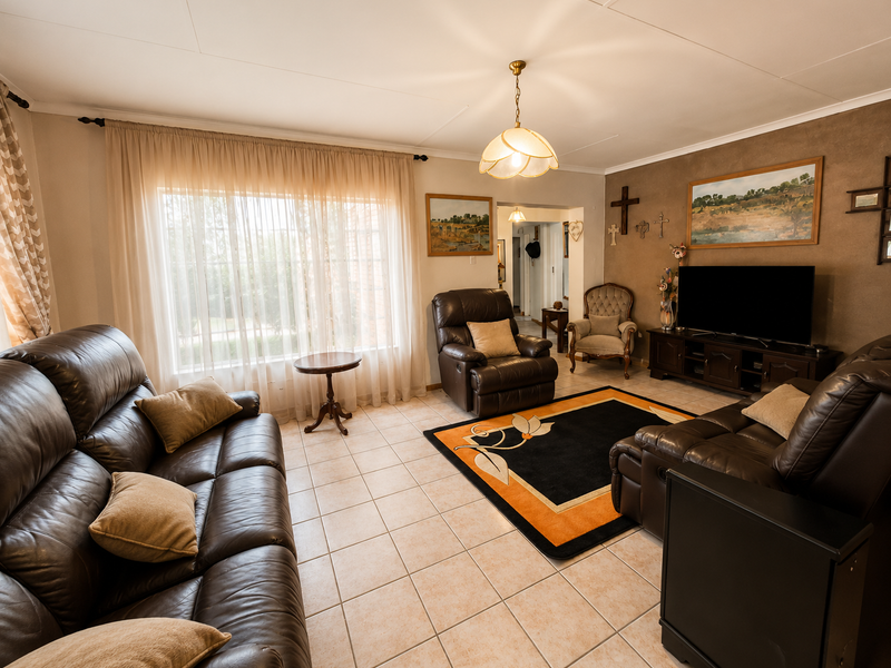 A spacious living room featuring tiled flooring, neutral wall tones, and natural light through large windows with sheer curtains.