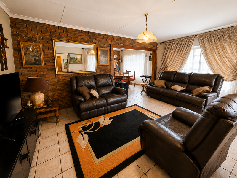 A spacious living room featuring an exposed brick feature wall, ceramic tiled flooring, and a coved ceiling, providing a warm and traditional atmosphere.