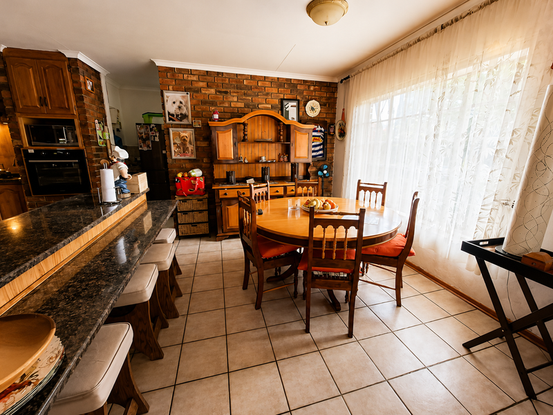 Open-plan dining and kitchen area featuring exposed brick walls, granite countertops, built-in appliances, and tiled flooring with natural light.