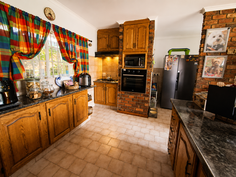 A traditional kitchen featuring wooden cabinetry, granite countertops, a built-in oven and microwave, and a distinctive exposed brick feature wall.