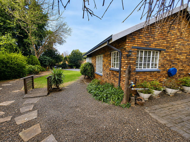 Rear view of a face brick house featuring a gravel pathway, a small wooden footbridge, and a well-maintained garden area.