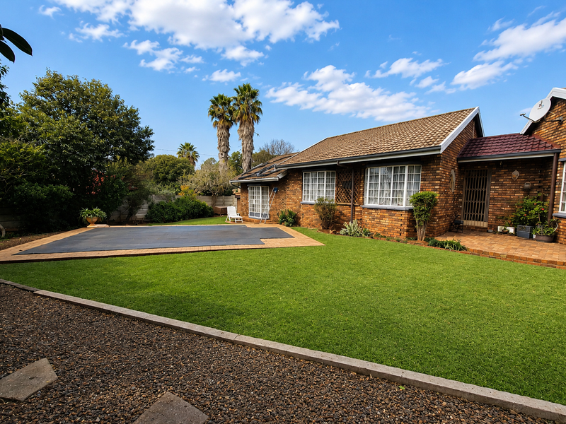 A well-maintained rear garden featuring a swimming pool with a cover, paved patio area, and classic brick facade house exterior.