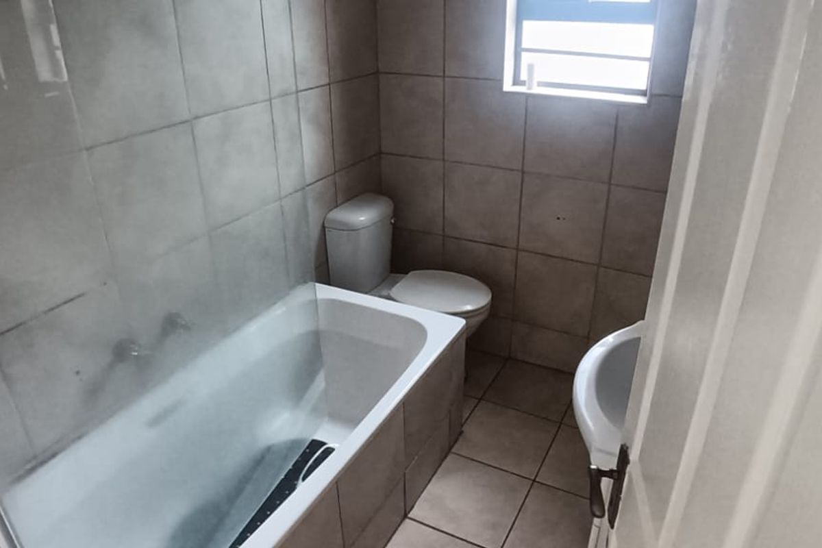 A functional bathroom featuring a built-in bathtub with a glass shower screen, a standard toilet, and tiled walls and flooring.