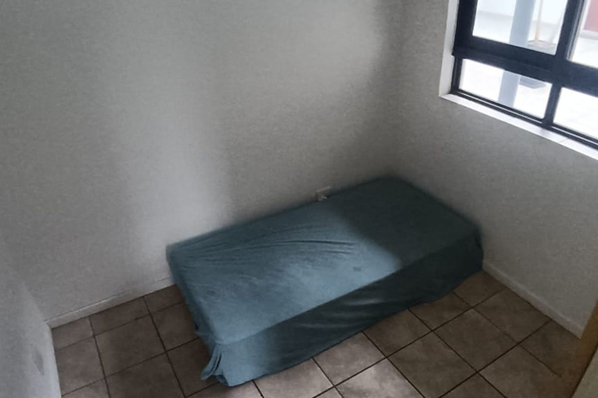 A compact bedroom featuring tiled flooring and a window with a dark frame, providing natural light to the space.