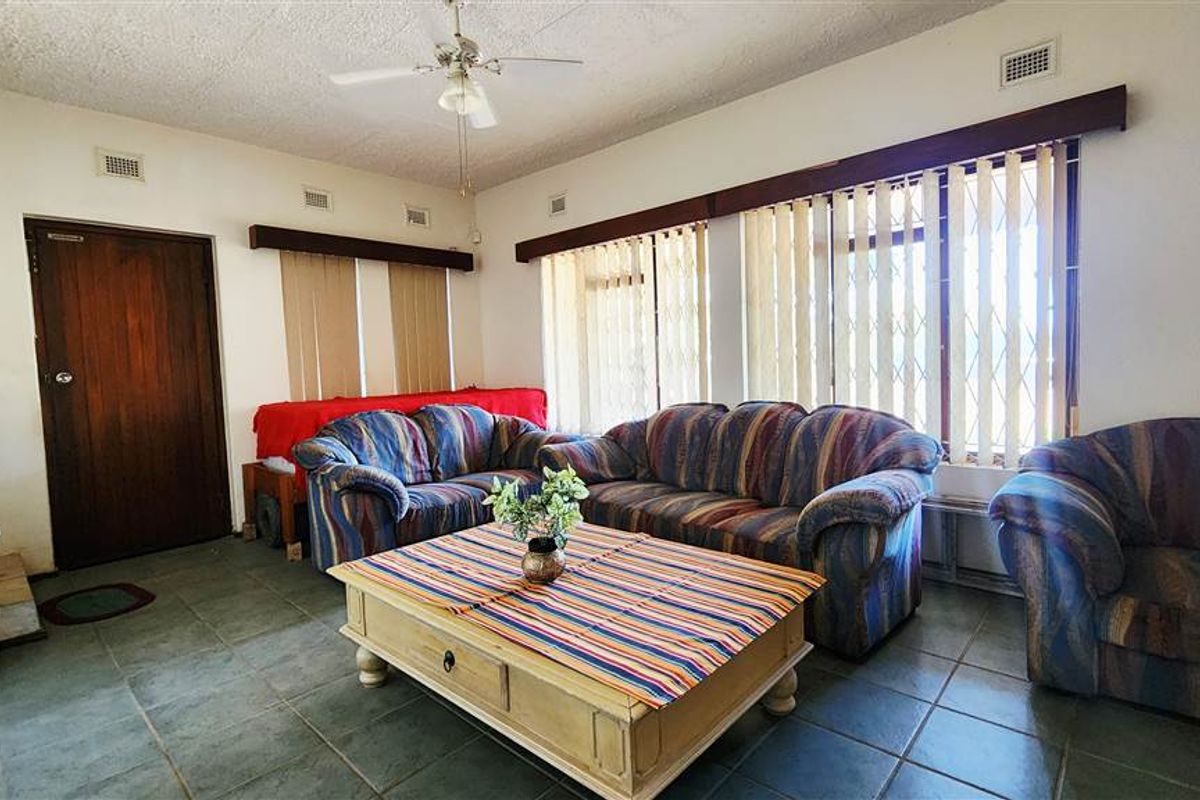 A spacious living room featuring large windows with vertical blinds, tiled flooring, and a ceiling fan, offering a functional and well-lit living area.