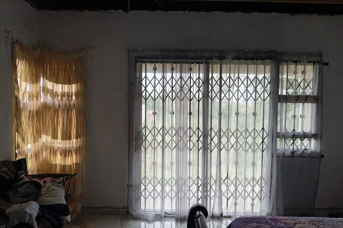A bedroom featuring tiled flooring and a sliding glass door secured with a metal security gate, leading to an outdoor area.