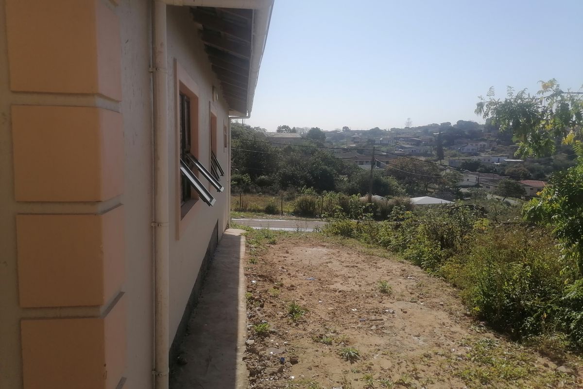 Side exterior view of the property showing the building facade, guttering, and an unlandscaped yard area with surrounding neighborhood views.