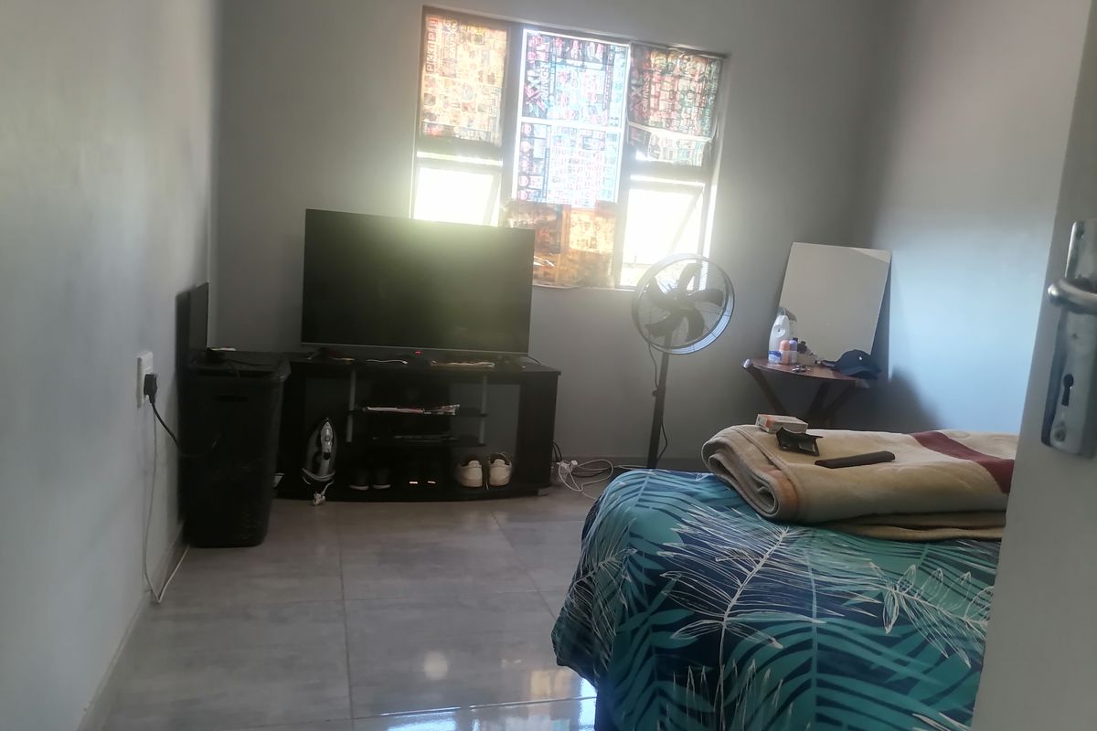 A simple bedroom featuring tiled flooring and a window with natural light.