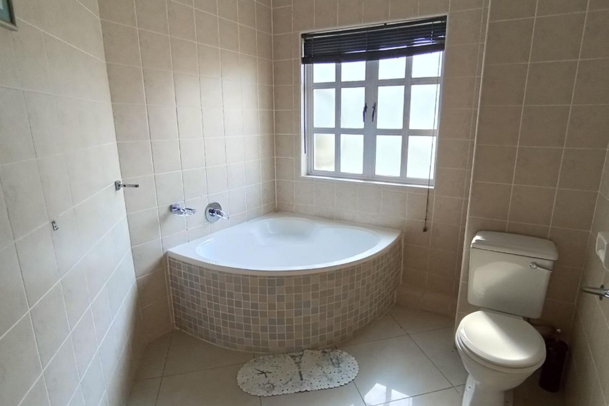 A functional bathroom featuring a corner bathtub with mosaic tiling, a standard toilet, and neutral wall tiles.
