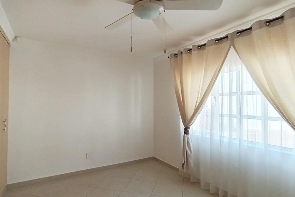A bright, empty bedroom featuring tiled flooring, built-in cupboards, and a ceiling fan, offering a clean and neutral space ready for personalization.