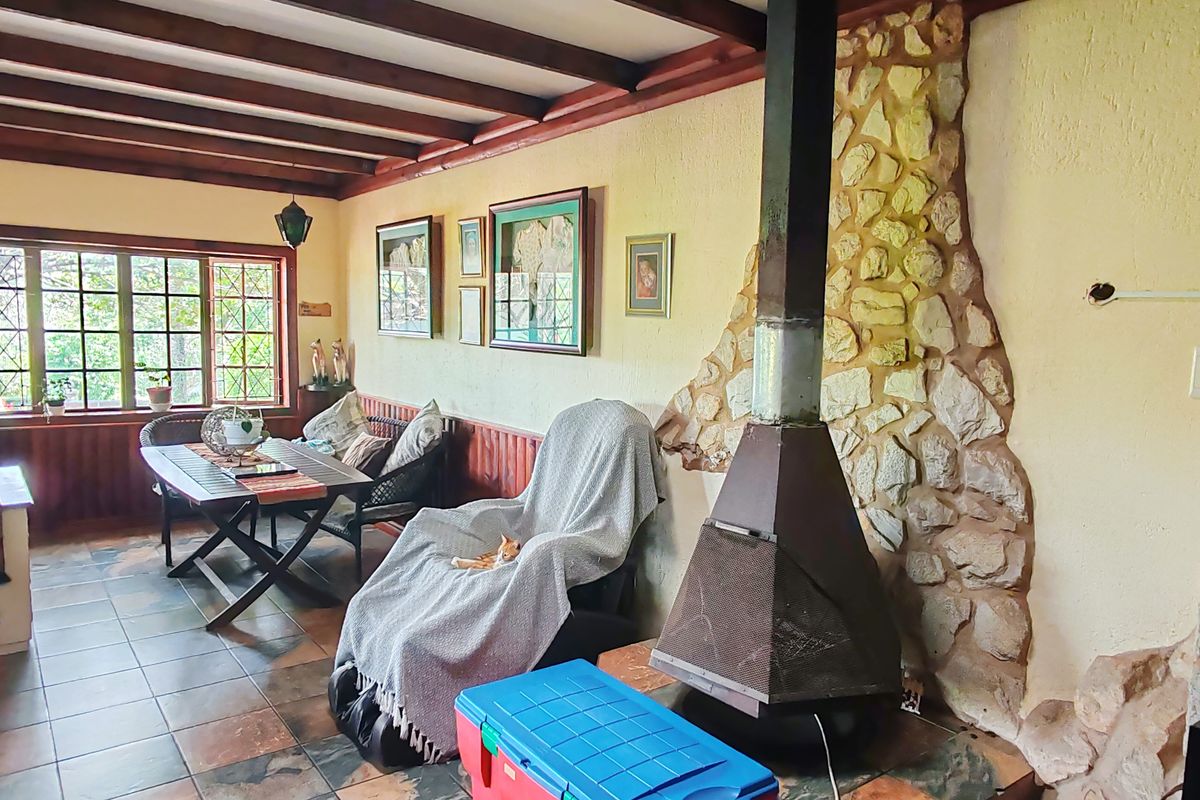 Living area featuring exposed timber ceiling beams, tiled flooring, and a prominent stone-clad fireplace with a metal flue.