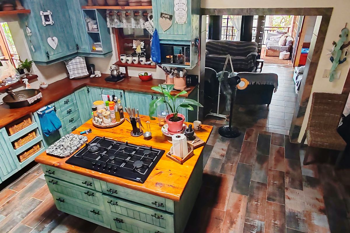 A rustic-style kitchen featuring a central island with a built-in gas hob, wooden countertops, and painted cabinetry, leading into an adjacent living area.