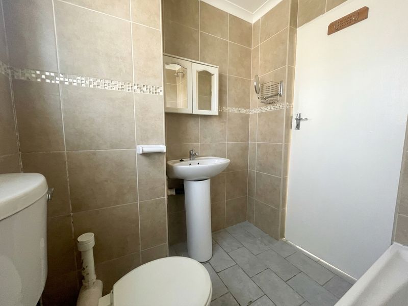 A functional bathroom featuring a pedestal basin, toilet, and wall-mounted medicine cabinet with neutral wall tiling and grey floor tiles.