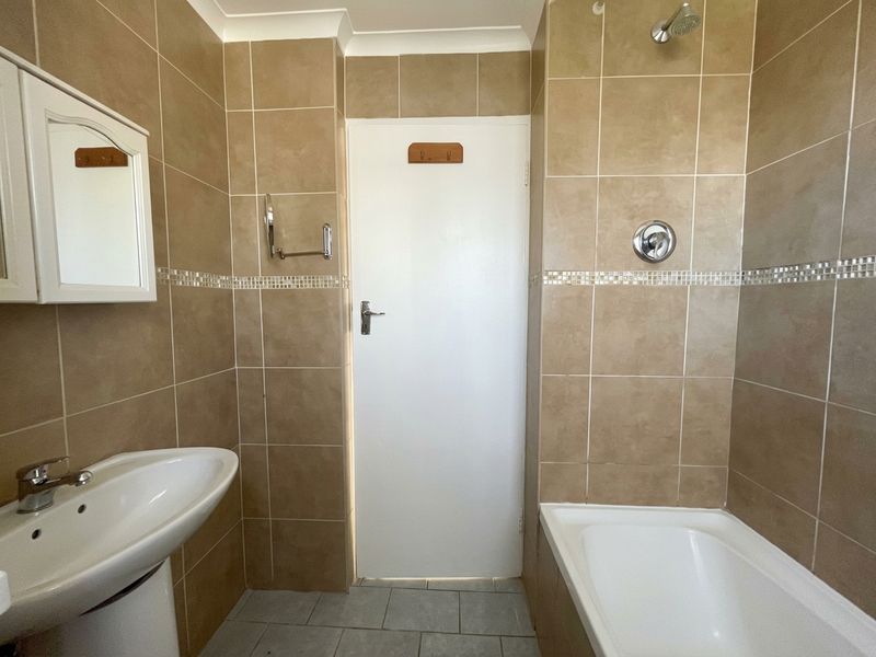 A functional bathroom featuring a pedestal basin, bathtub with shower head, and neutral wall tiling throughout.