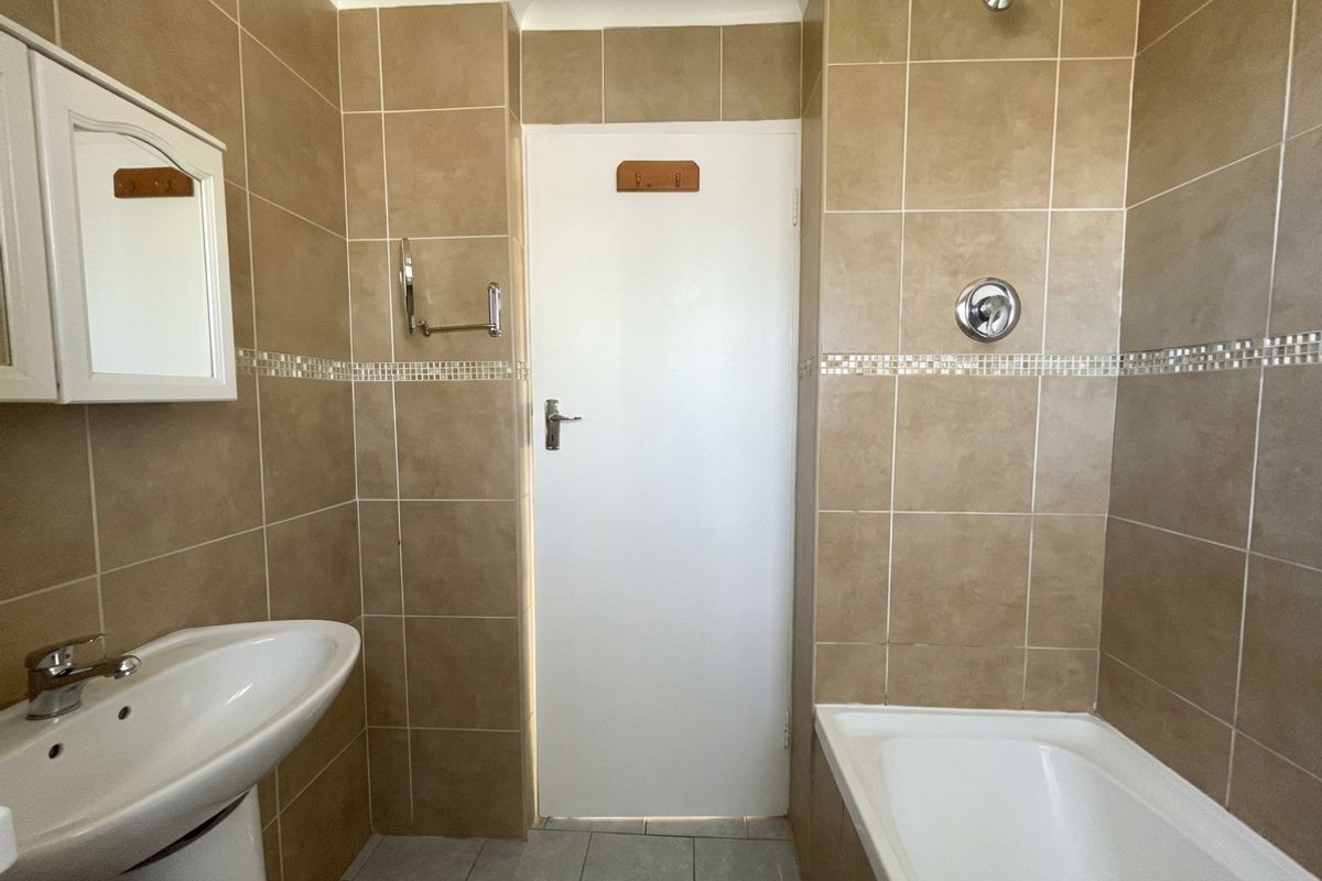 A functional bathroom featuring a pedestal basin, bathtub with shower head, and neutral wall tiling throughout.