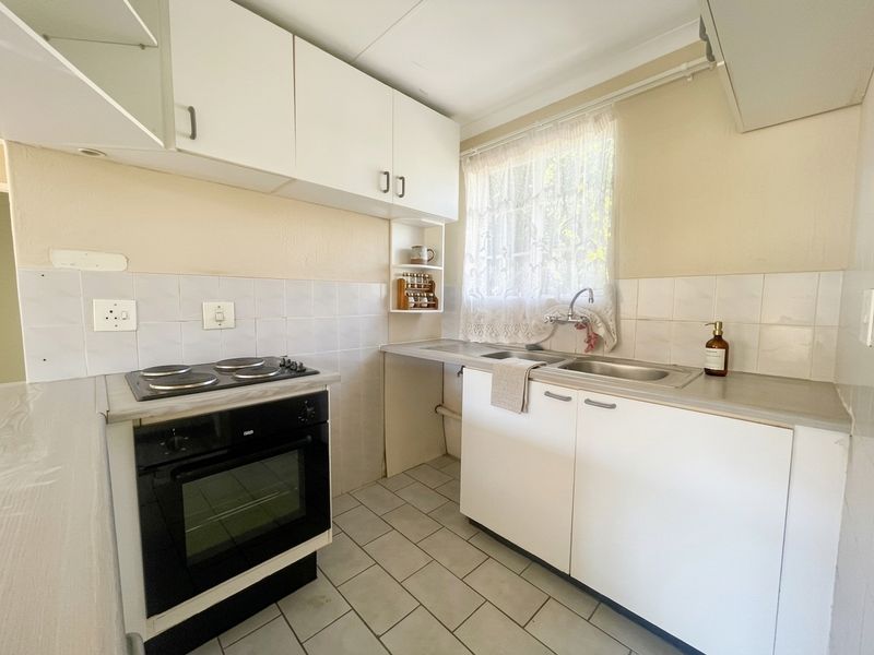A functional kitchen featuring white built-in cabinetry, an electric hob, an integrated oven, and a double sink with tiled splashbacks.