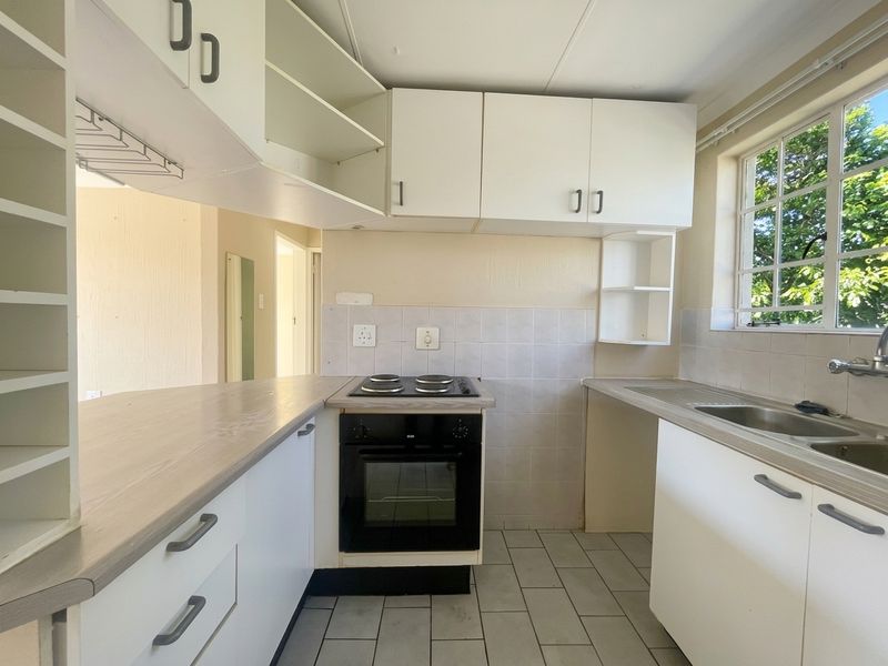 A functional, empty kitchen featuring white built-in cabinetry, laminate countertops, an integrated electric oven and hob, and a stainless steel sink.