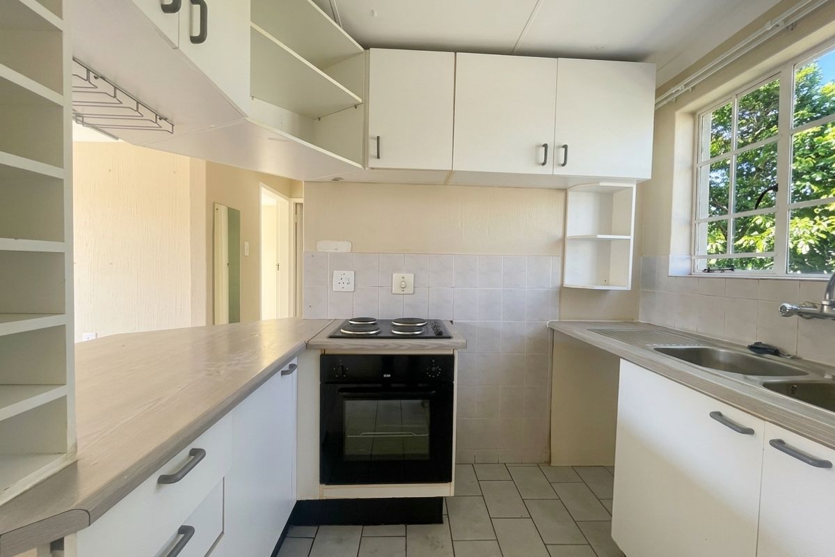 A functional, empty kitchen featuring white built-in cabinetry, laminate countertops, an integrated electric oven and hob, and a stainless steel sink.