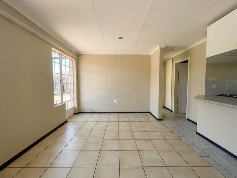 An open-plan living and kitchen area featuring neutral tiled flooring, recessed lighting, and a breakfast bar, offering a blank canvas for interior design.