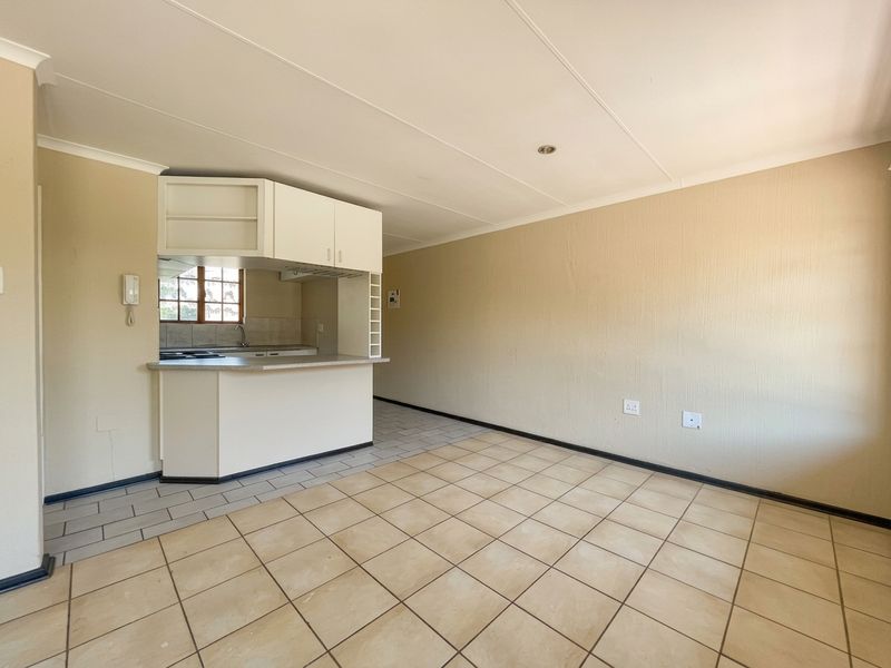An open-plan living and kitchen area featuring tiled flooring, built-in cabinetry, and a breakfast counter, offering a blank canvas for personalization.