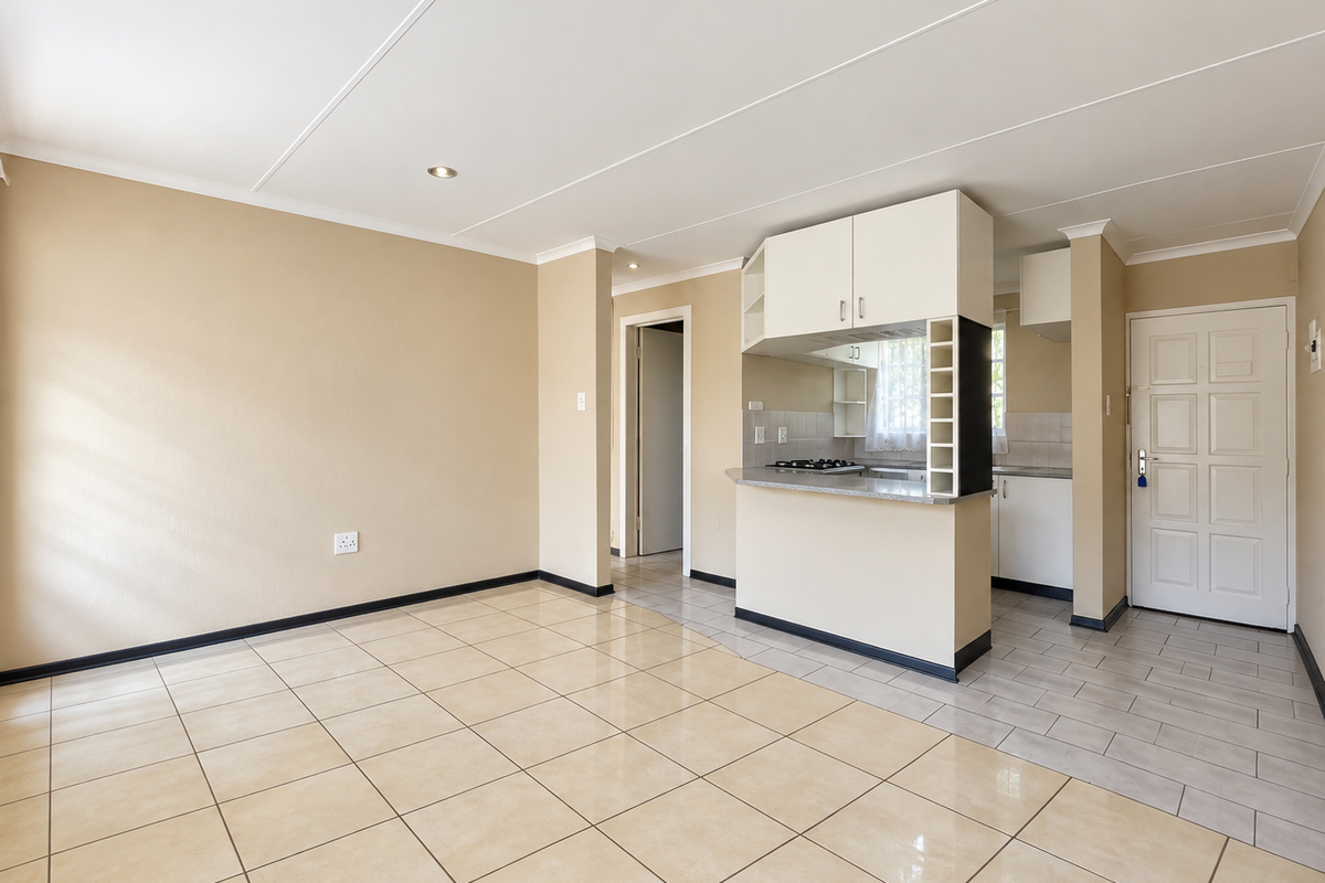 An open-plan living and kitchen area featuring neutral tiled flooring, recessed lighting, and a functional kitchen layout with built-in cabinetry and a breakfast counter.