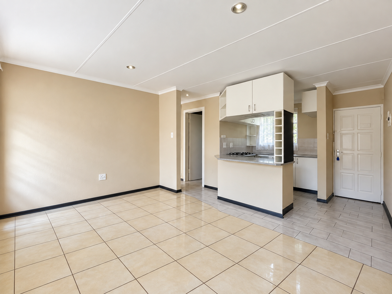 An open-plan living and kitchen area featuring neutral tiled flooring, recessed lighting, and a functional kitchen layout with built-in cabinetry and a breakfast counter.