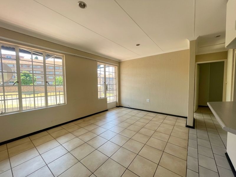 An empty open-plan living area featuring neutral tiled flooring, recessed lighting, and large windows providing natural light and access to the exterior.