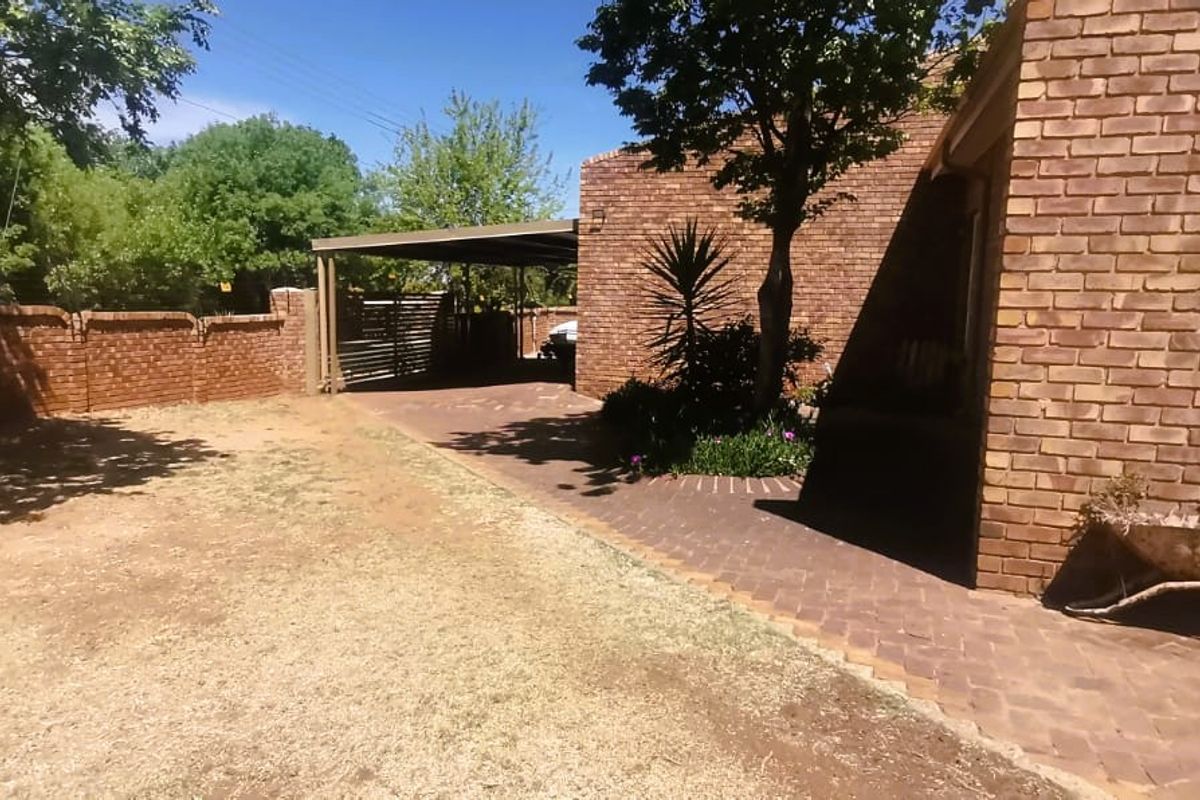 A rear exterior view of the property featuring a face brick facade, a paved driveway leading to a carport, and a surrounding boundary wall.