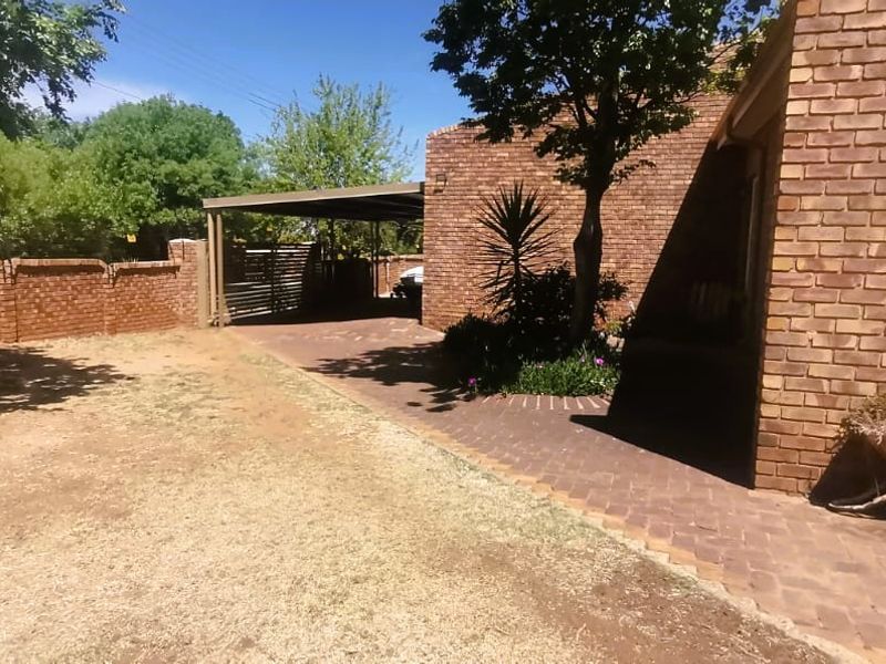 A rear exterior view of the property featuring a face brick facade, a paved driveway leading to a carport, and a surrounding boundary wall.