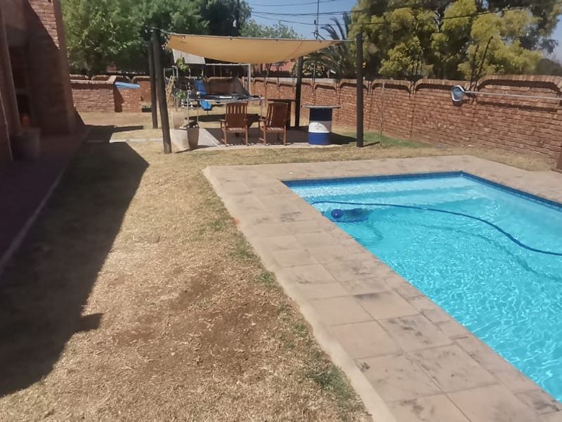 Outdoor pool area featuring a swimming pool, paved surround, and a shade sail structure, enclosed by a brick boundary wall.