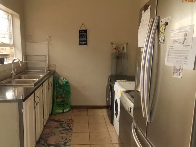 A functional scullery or laundry area featuring a double sink, tiled flooring, and dedicated plumbing connections for laundry appliances.