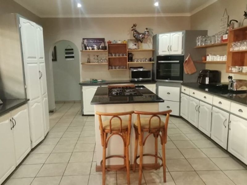 Spacious kitchen featuring a central island with a gas hob, granite countertops, ample white cabinetry, and open shelving, finished with tiled flooring.