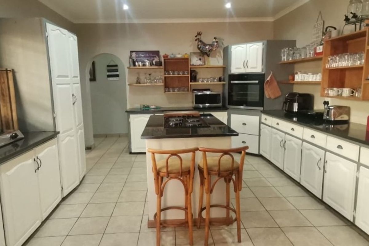 Spacious kitchen featuring a central island with a gas hob, granite countertops, ample white cabinetry, and open shelving, finished with tiled flooring.