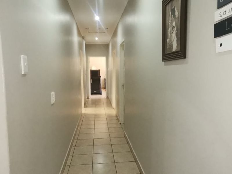 A clean, neutral-toned hallway featuring tiled flooring and recessed downlighting, providing a bright and functional transition space between rooms.