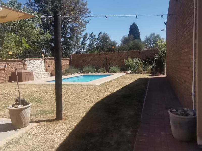 A private backyard featuring a swimming pool, brick boundary walls, and a paved walkway alongside the house exterior.