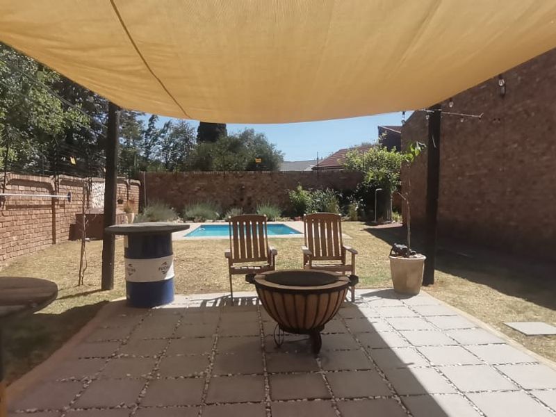 Outdoor patio area featuring a shade sail, paved flooring, and a brick boundary wall, overlooking a private swimming pool and garden.