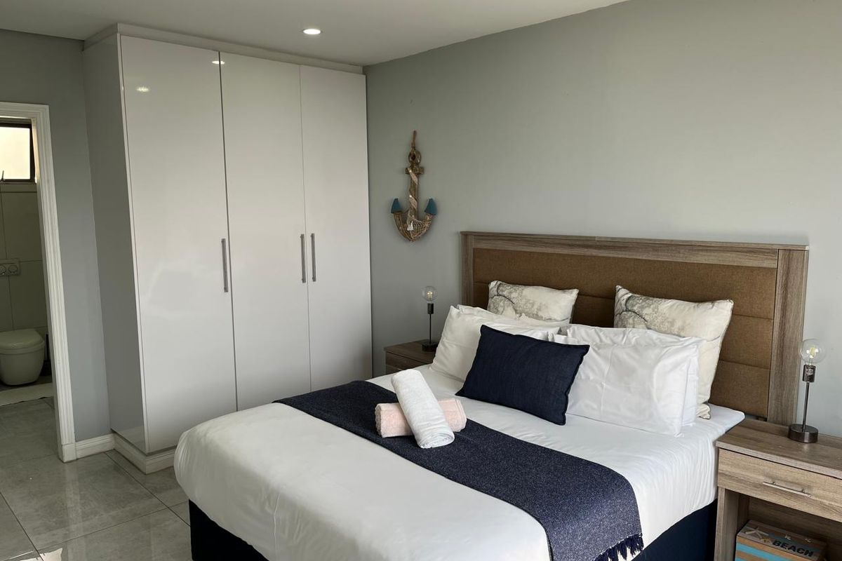 A well-maintained bedroom featuring modern built-in wardrobes, recessed downlighting, and sleek tiled flooring, with an adjoining en-suite bathroom visible.