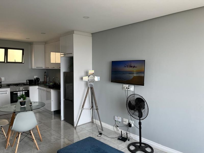Modern open-plan living area featuring a sleek kitchen with built-in cabinetry, gas hob, and tiled flooring, seamlessly flowing into the adjacent living space.