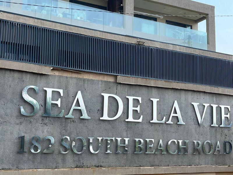 Exterior view of the Sea De La Vie apartment building facade featuring modern signage and glass balcony balustrades.