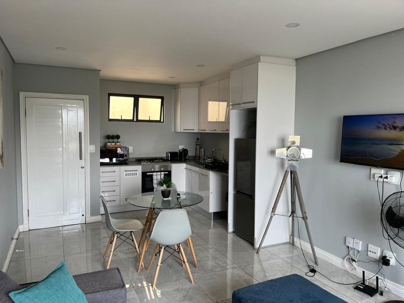 Modern open-plan living area featuring a compact kitchen with white cabinetry, gas hob, and tiled flooring, seamlessly integrated with the dining and lounge space.